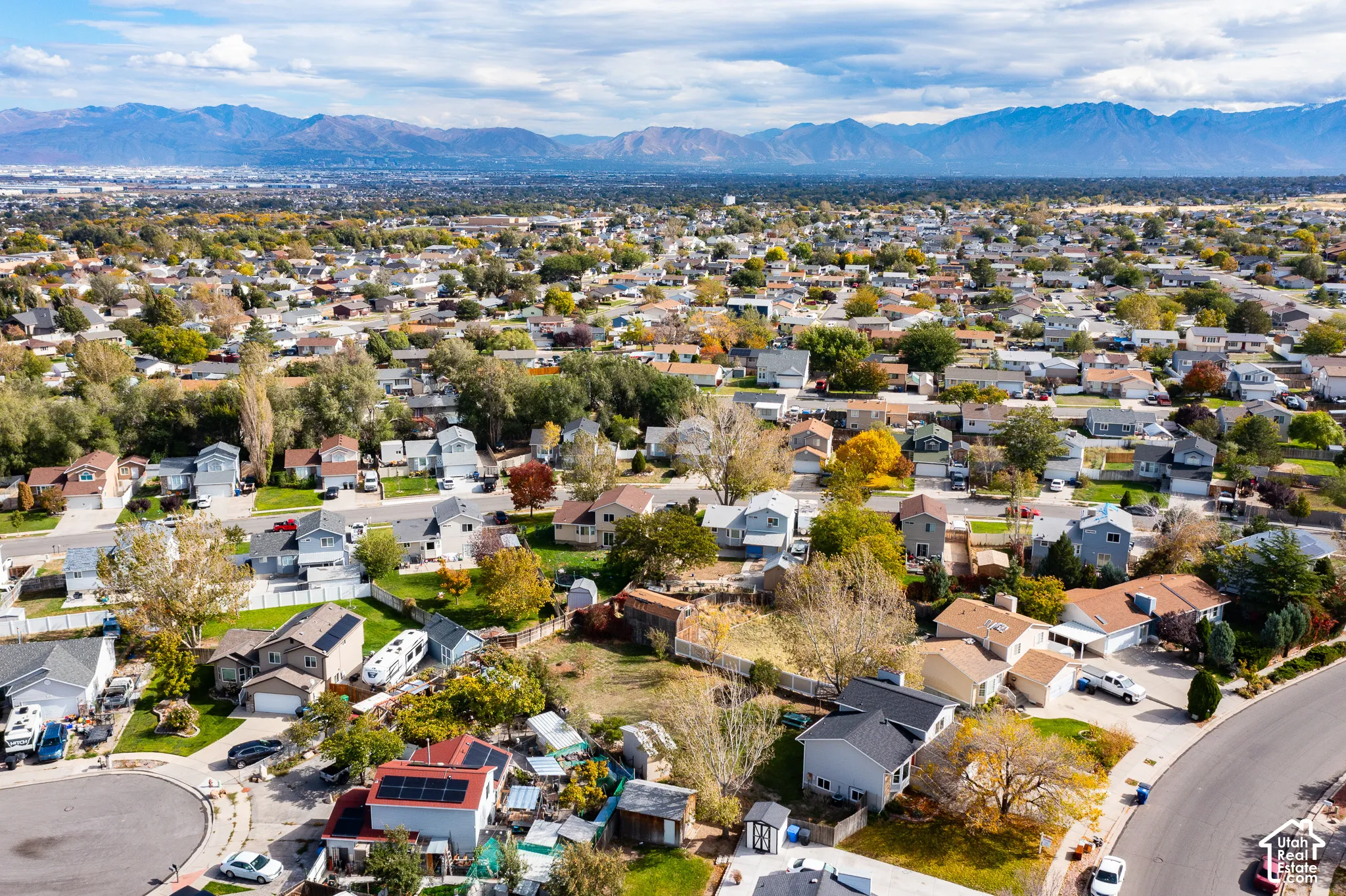 Aerial perspective showcasing a residential neighborhood featuring mountain topography, mature trees, varied roof pitches, and established street infrastructure