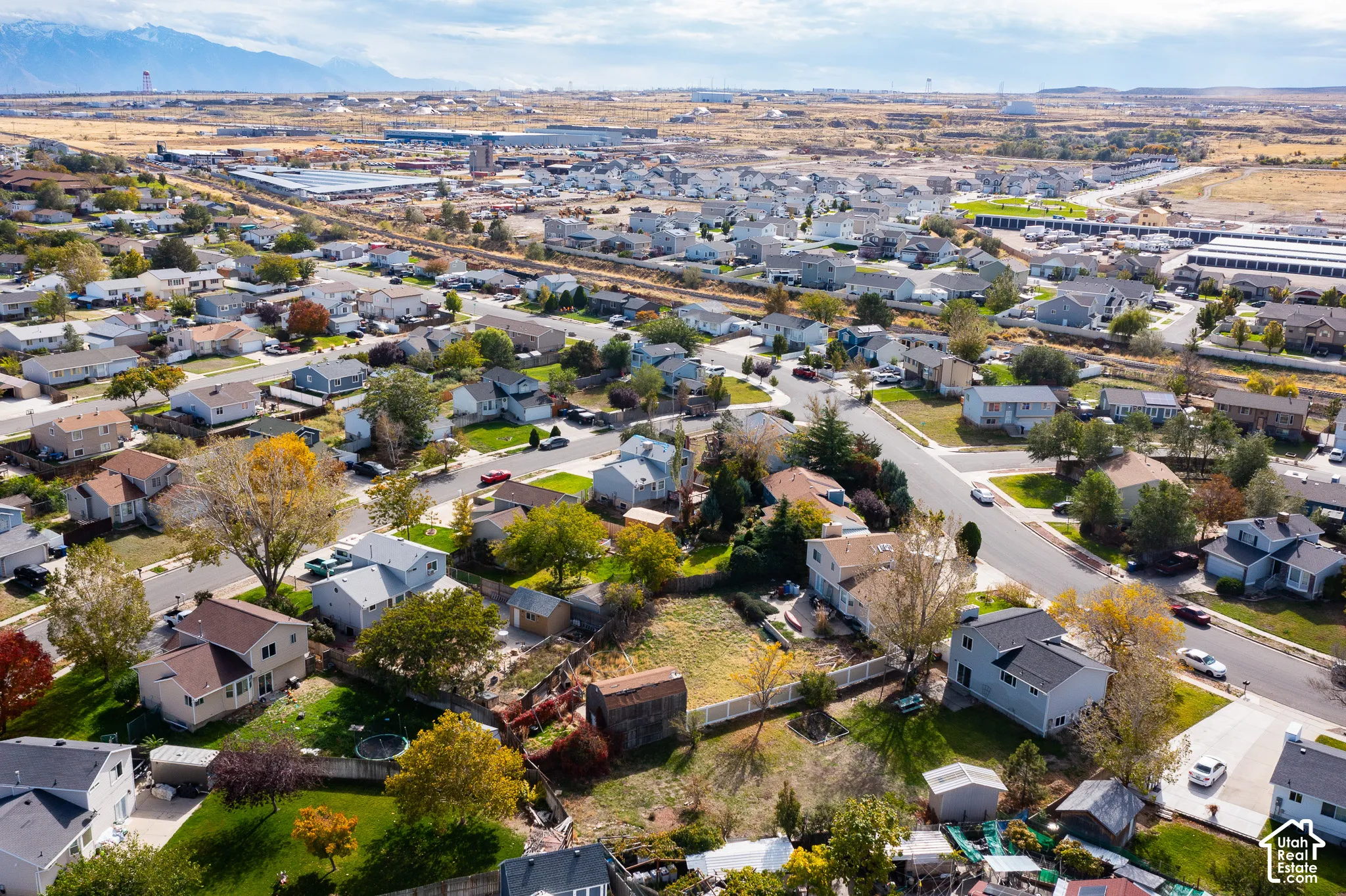 Aerial perspective of suburban residential neighborhood featuring mature trees, manicured lawns, fenced backyards, and mountain range backdrop
