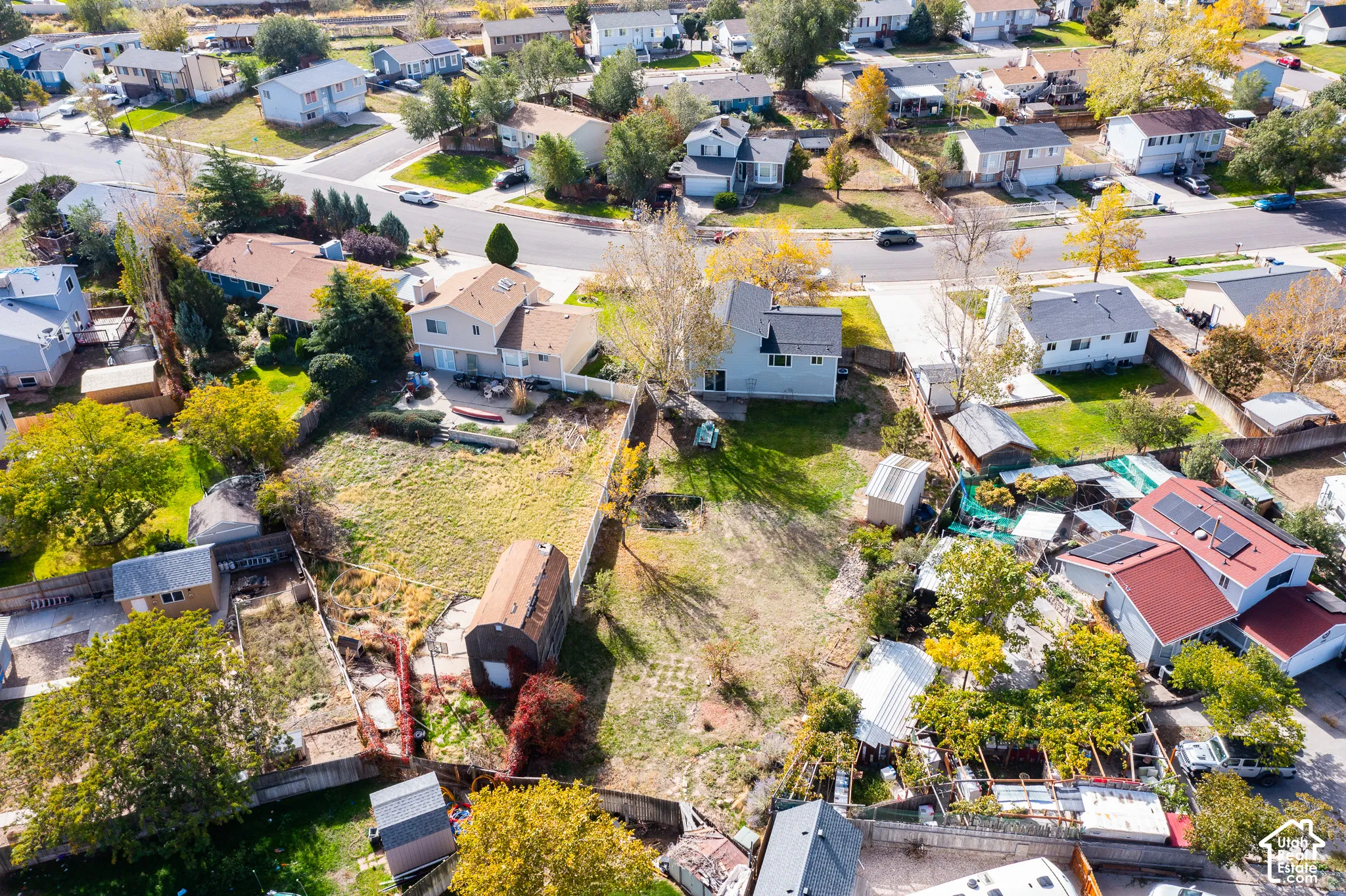 Aerial perspective of a multi-level suburban property featuring an expansive backyard, detached storage structure, wooden perimeter fencing, and mature trees