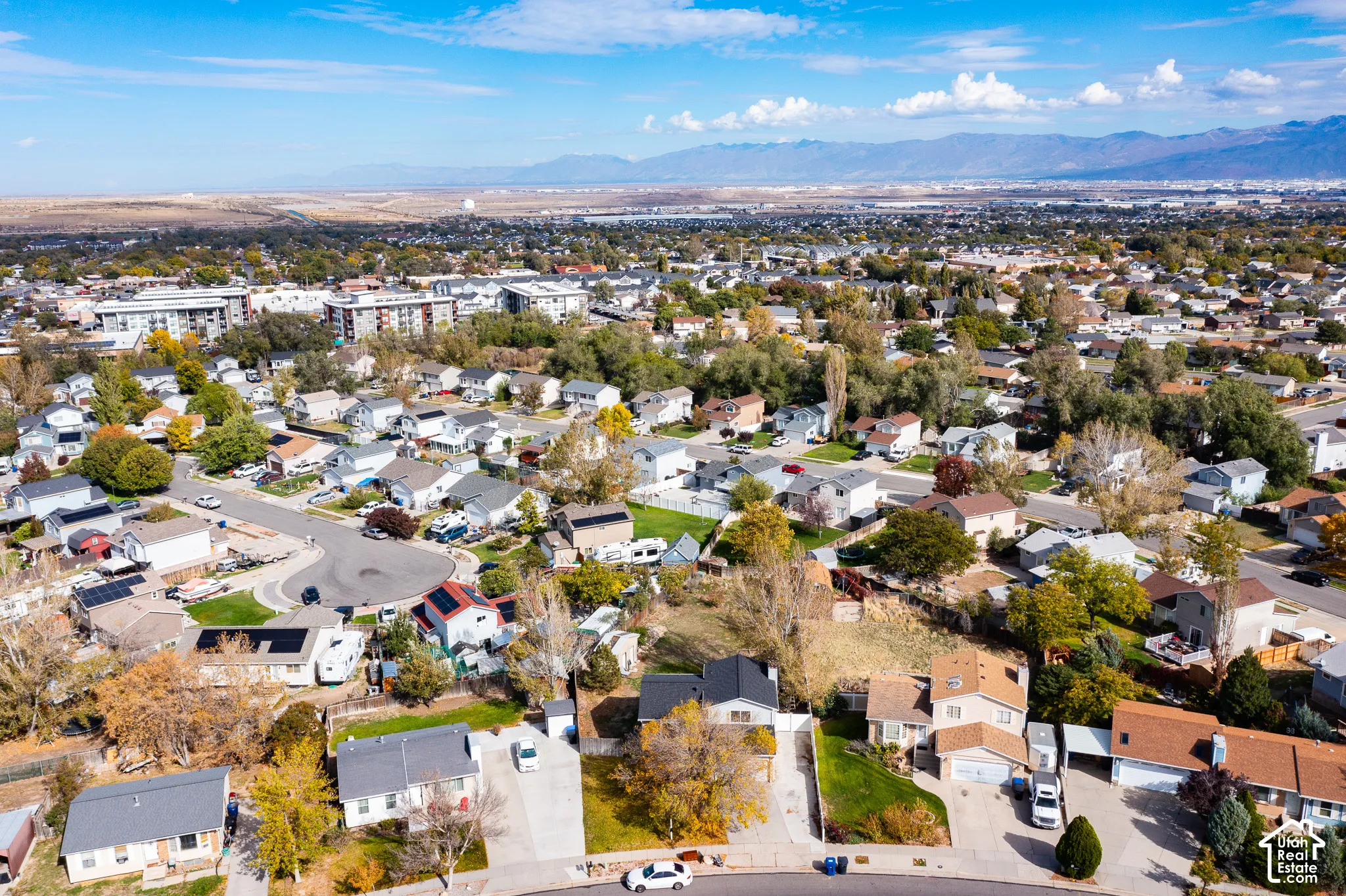 Aerial perspective featuring residential lots with concrete driveways, mature trees, and distant mountain topography