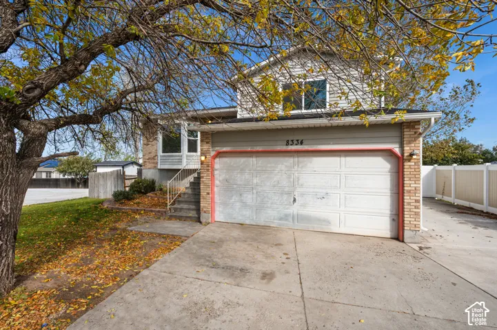 Split-level exterior featuring light brick masonry, horizontal siding, an attached two-car garage, and concrete driveway