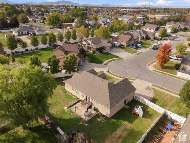 Aerial perspective of residential property featuring a sprawling lawn, backyard patio, white vinyl perimeter fencing, and established trees