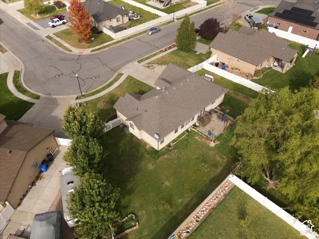 Aerial perspective featuring a corner lot, paved concrete driveway, expansive rear lawn, stone-paver patio, and white vinyl privacy fencing
