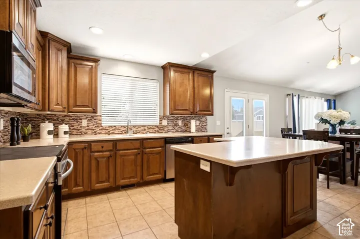 Kitchen featuring stained wood cabinetry, stone-tiled backsplash, central island with an extended countertop, stainless steel appliances, and ceramic tile flooring