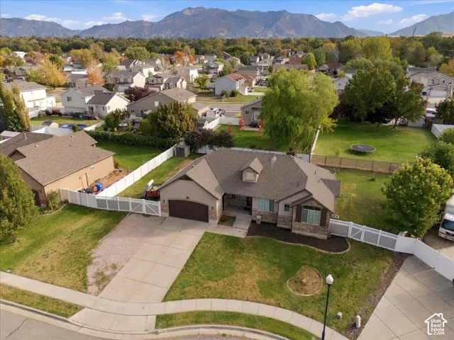 Single-story residence featuring a multi-gabled shingle roof, stone and stucco siding, an attached two-car garage, white vinyl perimeter fencing, and a mountain backdrop