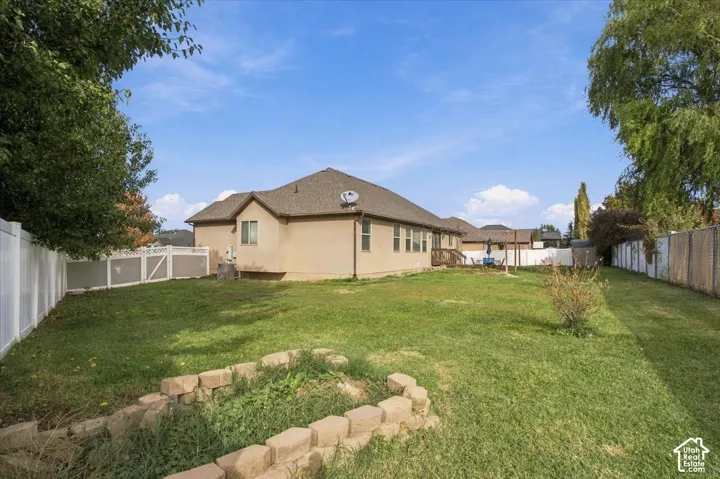 Expansive backyard featuring a manicured lawn, stone retaining wall, perimeter vinyl fencing, and mature trees