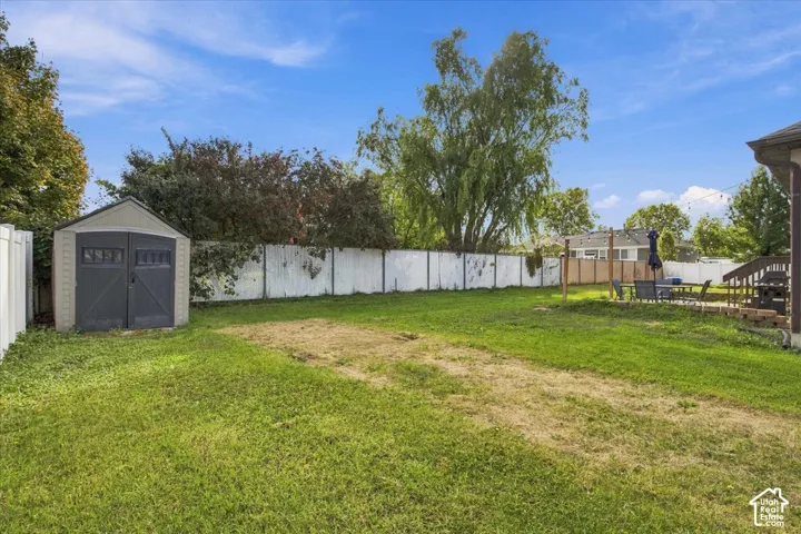 Rear yard featuring a grass lawn, perimeter vinyl fencing, and a detached storage shed