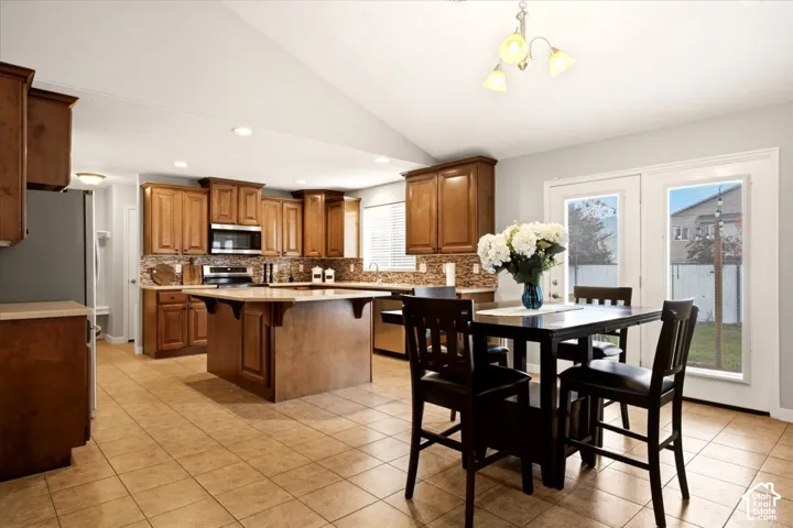 Kitchen featuring wood cabinetry, a central island with countertop seating, stone tile backsplash, and tile flooring under a vaulted ceiling