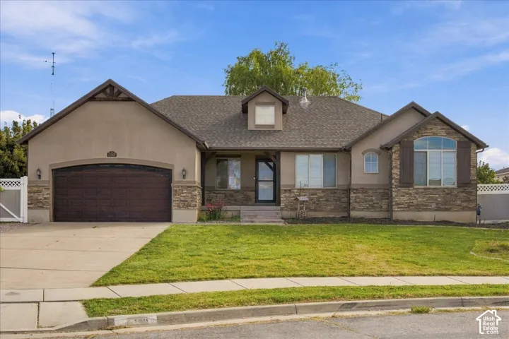 Single-level residence featuring a stucco and stone exterior, attached two-car garage, asphalt shingle roof, arched window detail, and covered entryway