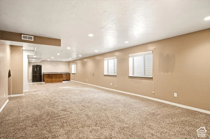 Open interior space featuring recessed lighting, carpeted flooring, two egress-style windows, and a built-in wet bar with cabinetry
