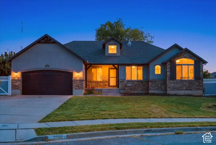 Stucco and stone veneer exterior featuring an arched garage door, gabled roofline, dormer window, and covered entry