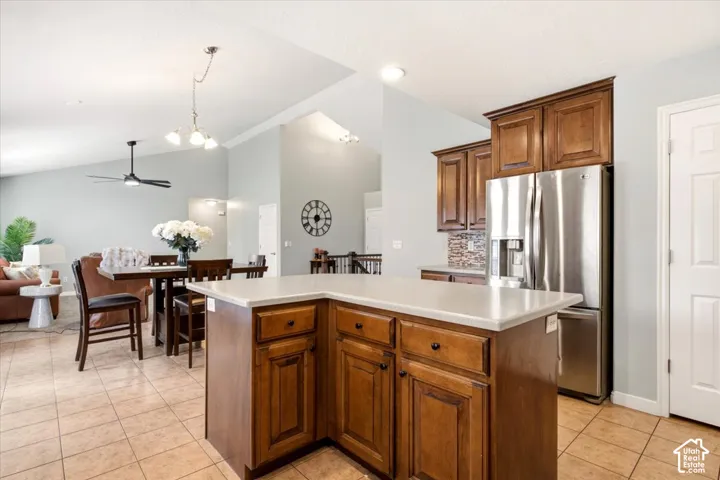 Kitchen featuring stained wood cabinetry, stone-composite countertops, stainless steel refrigerator, tile flooring, and vaulted ceilings