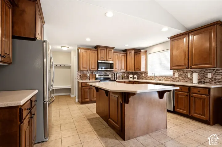 Kitchen featuring wood cabinetry, a central island with a breakfast bar, tile flooring, recessed lighting, and a multi-tone tile backsplash