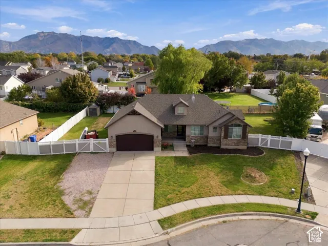 Single-story residence featuring a multi-gable roofline, stone veneer accents, an attached two-car garage, white vinyl perimeter fencing, and mountain scenery
