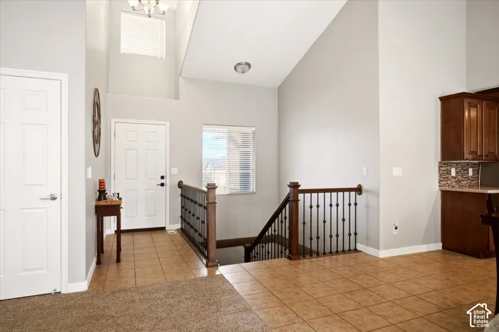 Vaulted ceilings, neutral wall tones, tile flooring, and a staircase featuring a wood handrail with metal balusters