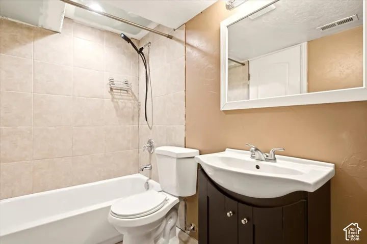 Bathroom featuring a dark-finish vanity with a white basin, chrome-finish dual-handle faucet, wall-mounted rectangular mirror, and a tile-surround shower and tub combination