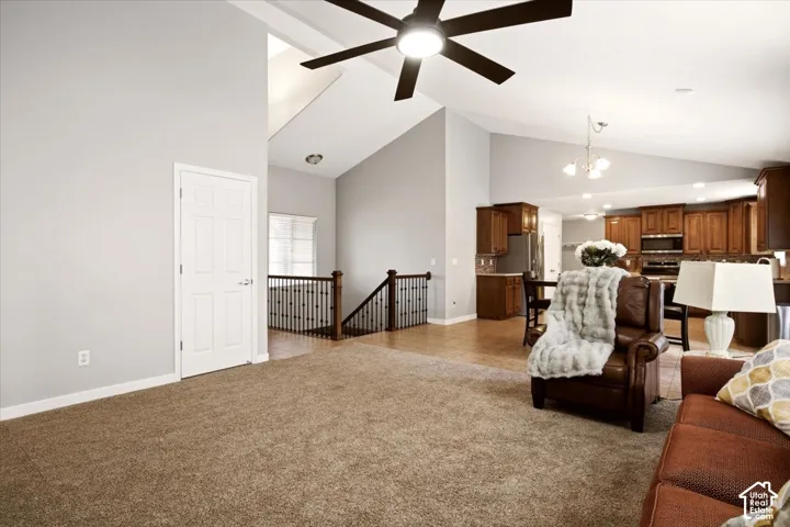 Vaulted ceilings featuring a modern ceiling fan, staircase with decorative metal balusters, and kitchen cabinetry with integrated stainless steel appliances