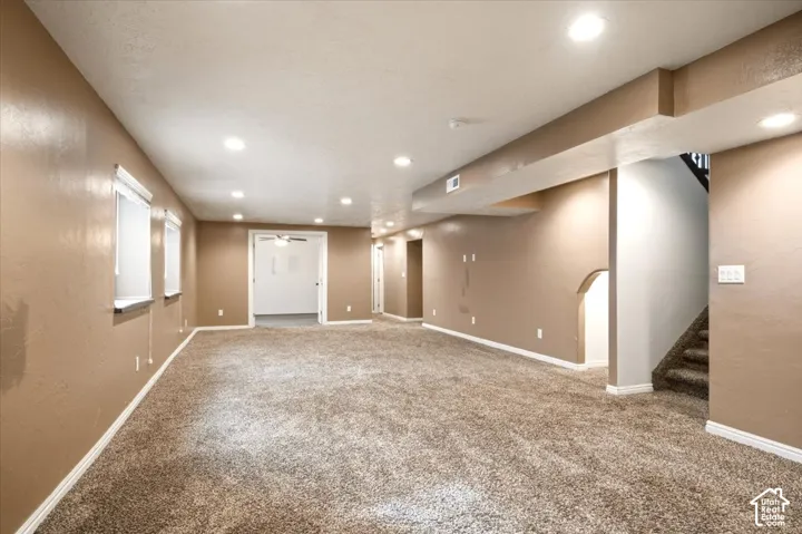 Expansive interior space featuring neutral wall tones, recessed lighting, wall-to-wall carpeting, and an open staircase with carpeted treads