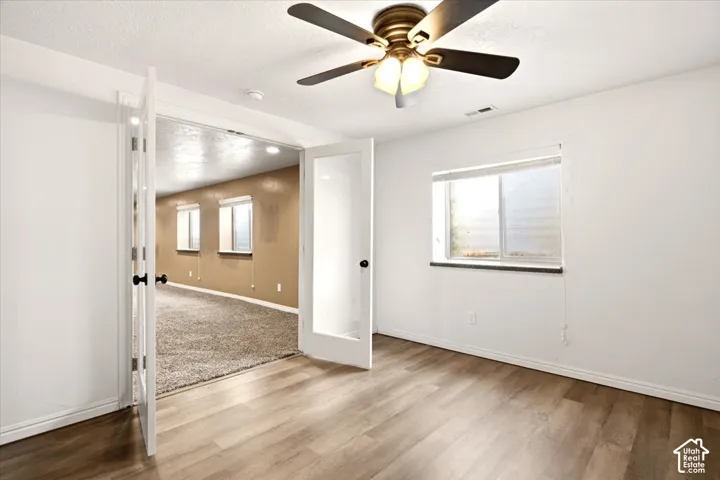 Room featuring wood-finish flooring, glass-paneled double doors, and a ceiling-mounted light fixture with a central fan