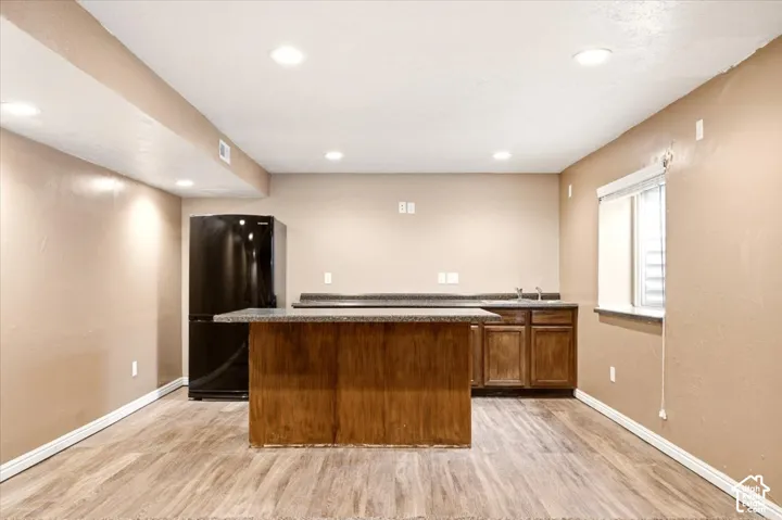 Kitchenette featuring wood-finish cabinetry, a central island with a stone-finish countertop, a black refrigerator, recessed lighting, and wood-finish flooring