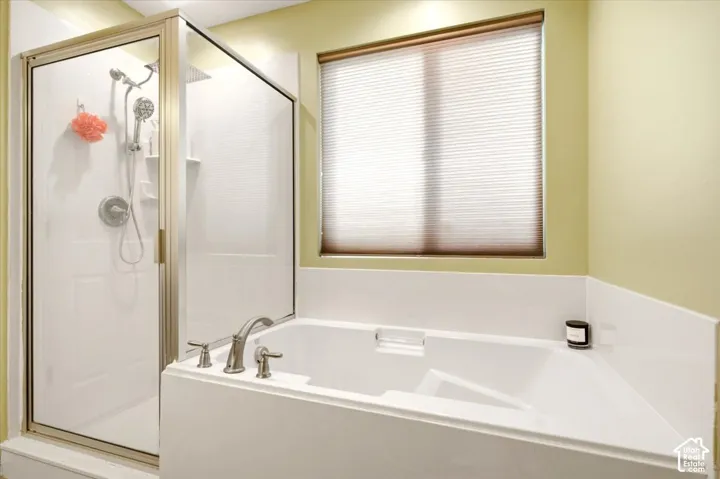Bathroom featuring a white soaking tub with deck-mounted faucet, separate shower enclosure with metal framing, handheld showerhead, and integrated shelving