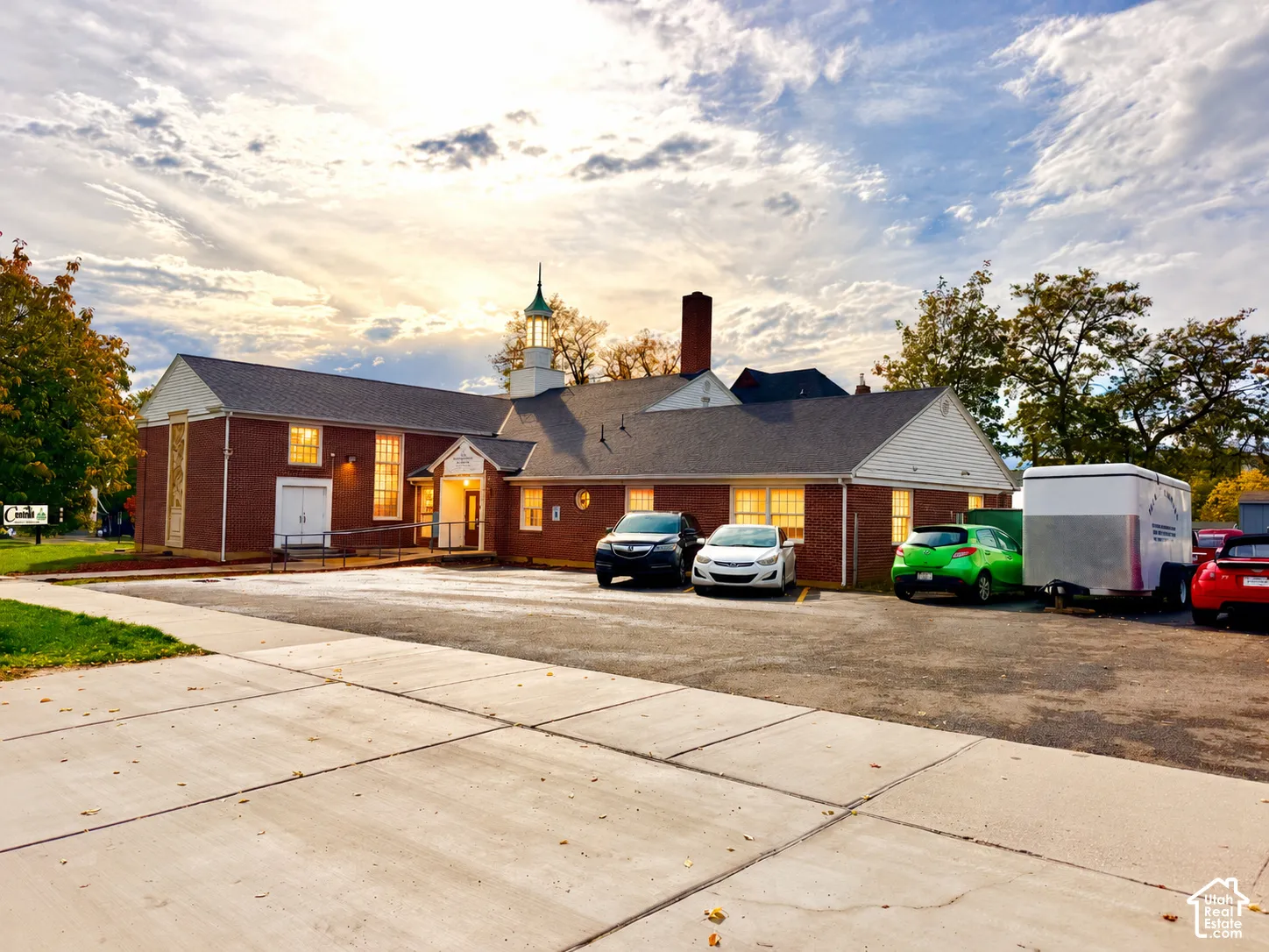 Brick exterior facade featuring a central cupola, gabled roofline, multi-pane windows, and dedicated asphalt parking area