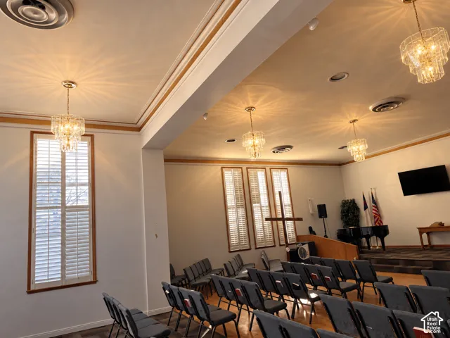 Spacious assembly hall featuring multi-tiered crystal chandeliers, crown molding, plantation shutters, and a raised platform area