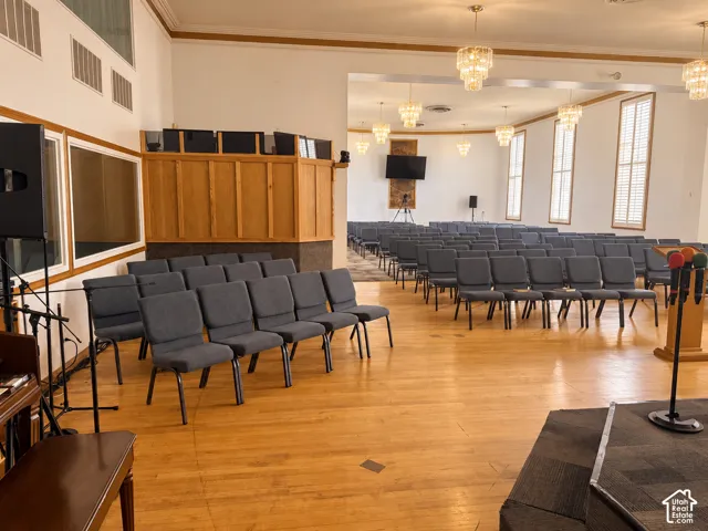 Spacious assembly hall featuring wood-finish flooring, multi-tiered crystal chandeliers, crown molding, and tall vertical windows