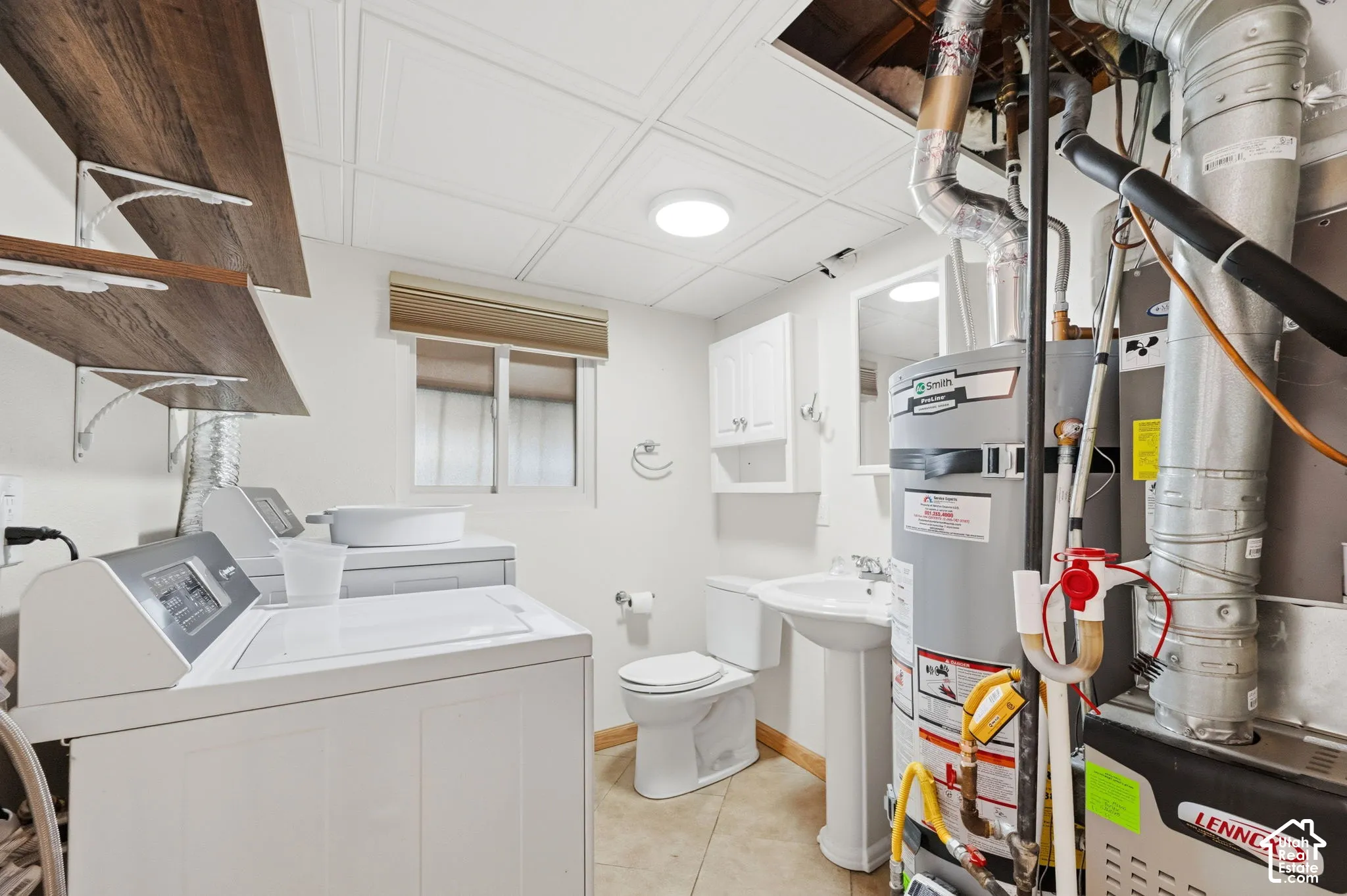 Utility area and half bath featuring tile flooring, a toilet, pedestal sink, and wall-mounted cabinet