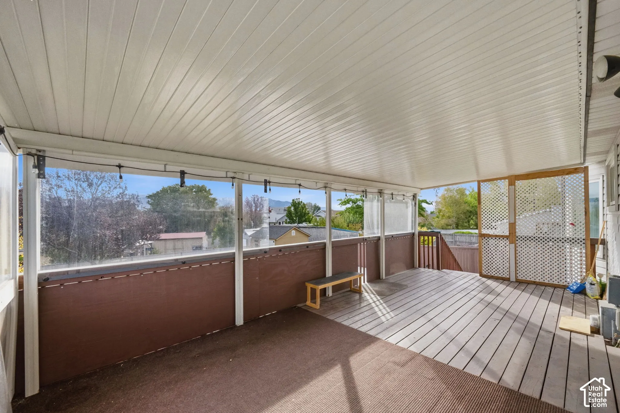 Covered deck featuring wood-plank flooring, a high-sloped ceiling, partial screening, and decorative lattice panels