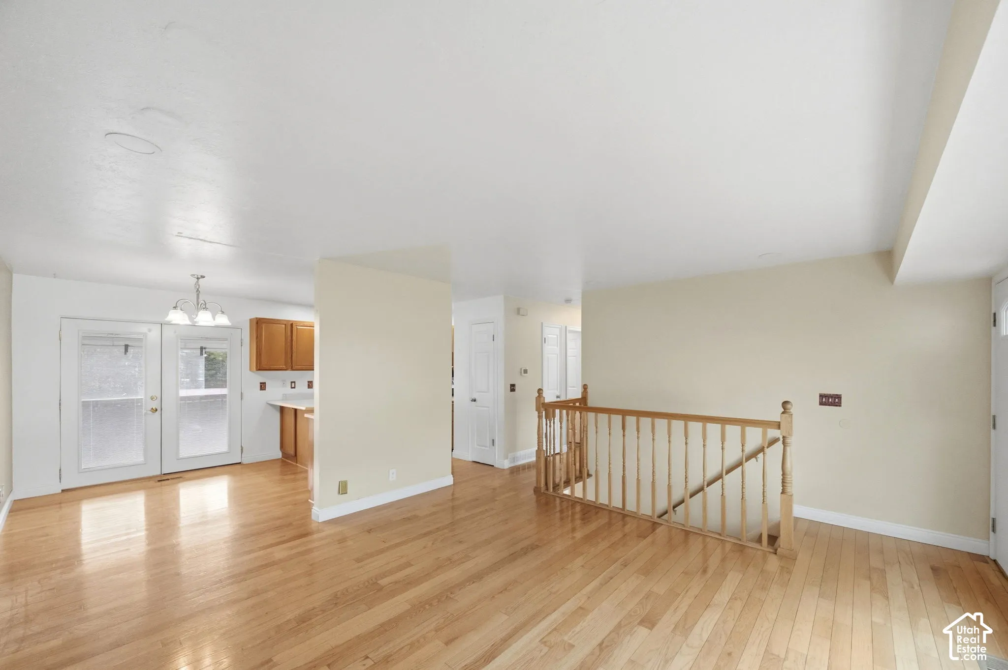 Open-concept interior featuring wood-finish flooring, a wood-railing staircase, double glass-panel doors, and natural wood cabinetry