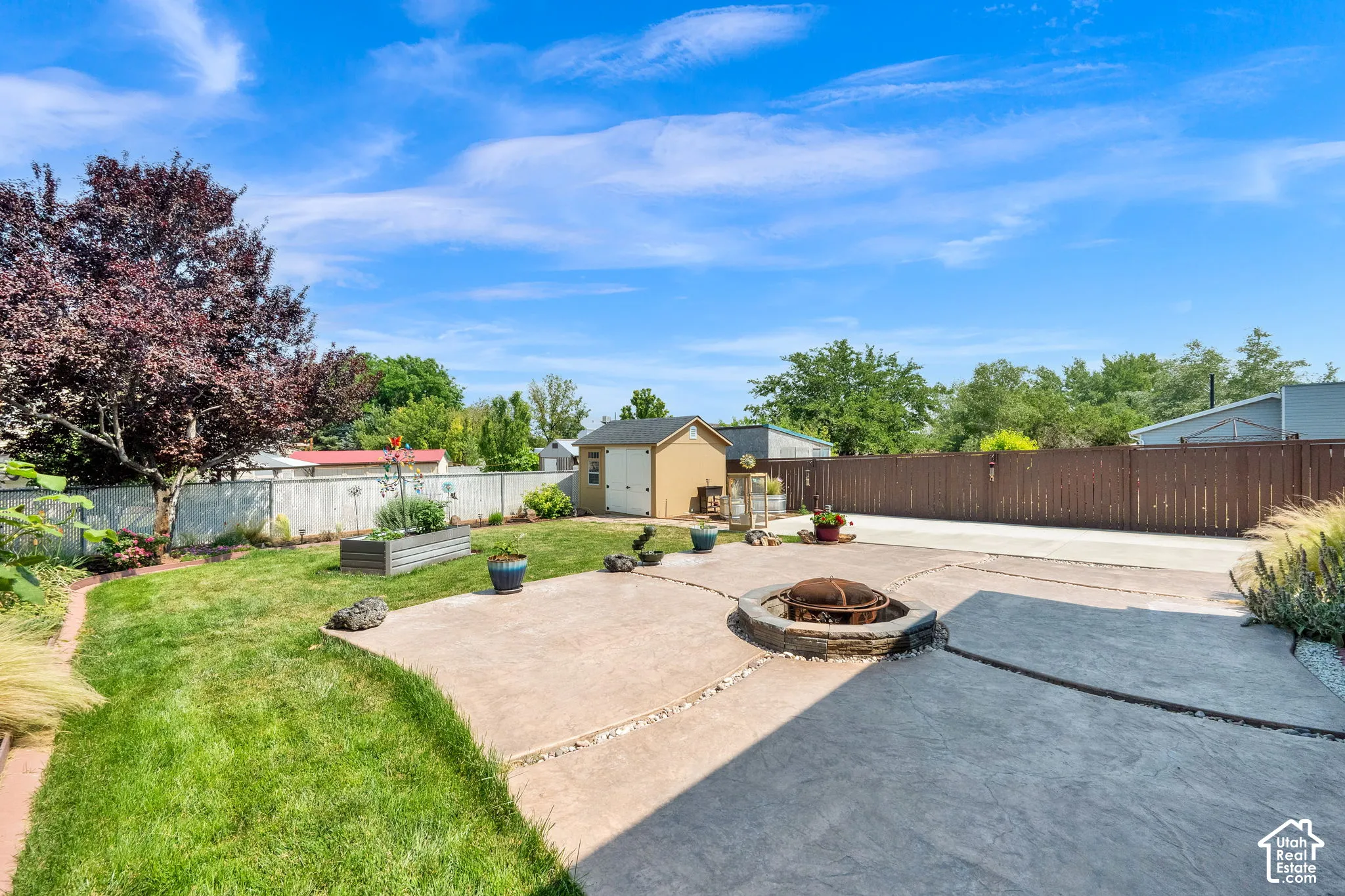 Backyard featuring a stamped concrete patio, stone-rimmed fire pit, lawn area, storage shed, and wood fencing
