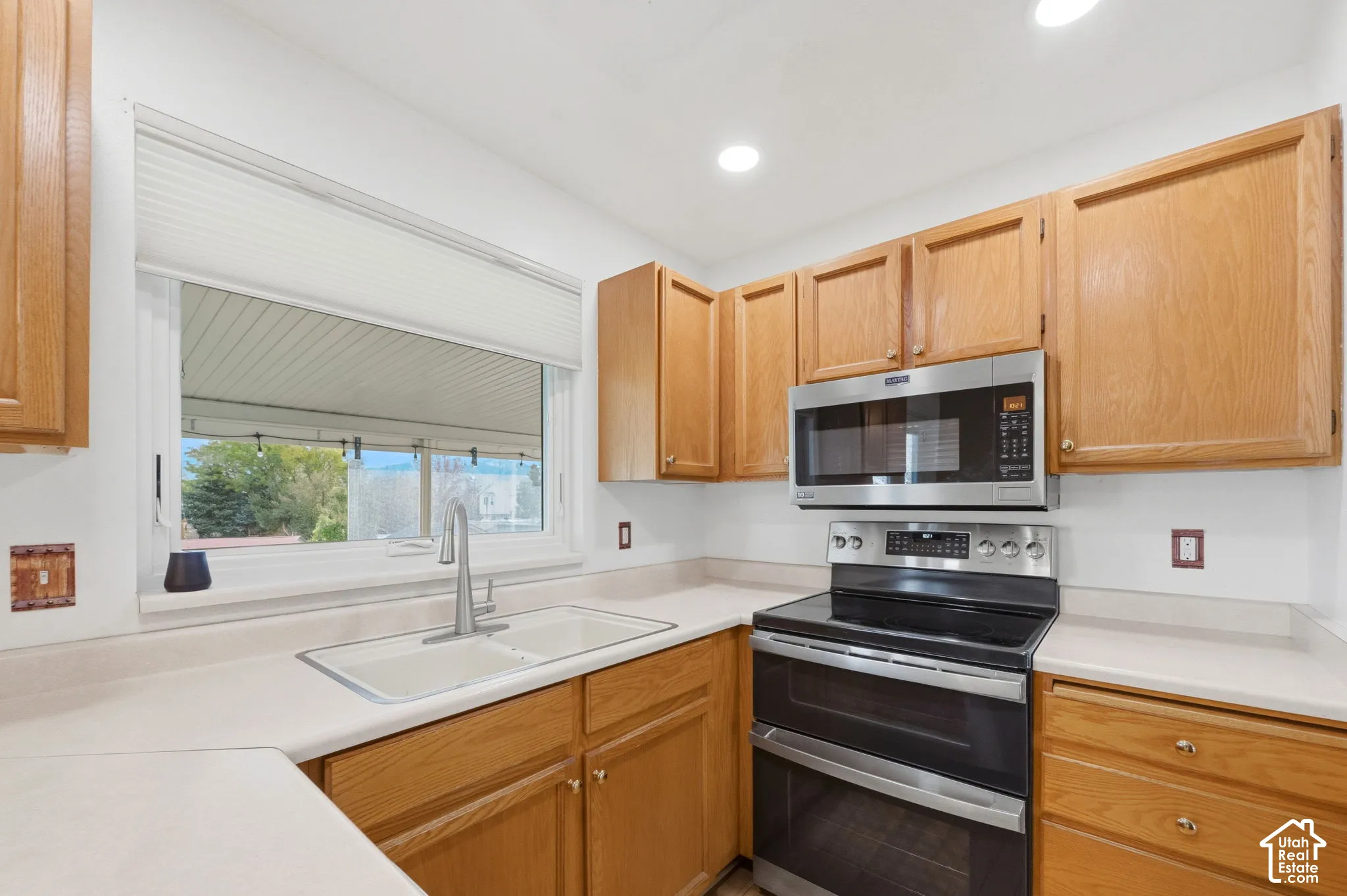 Kitchen featuring natural wood cabinetry,  stainless steel dual-oven range, built-in microwave, and a stainless steel dual-basin sink with a gooseneck faucet