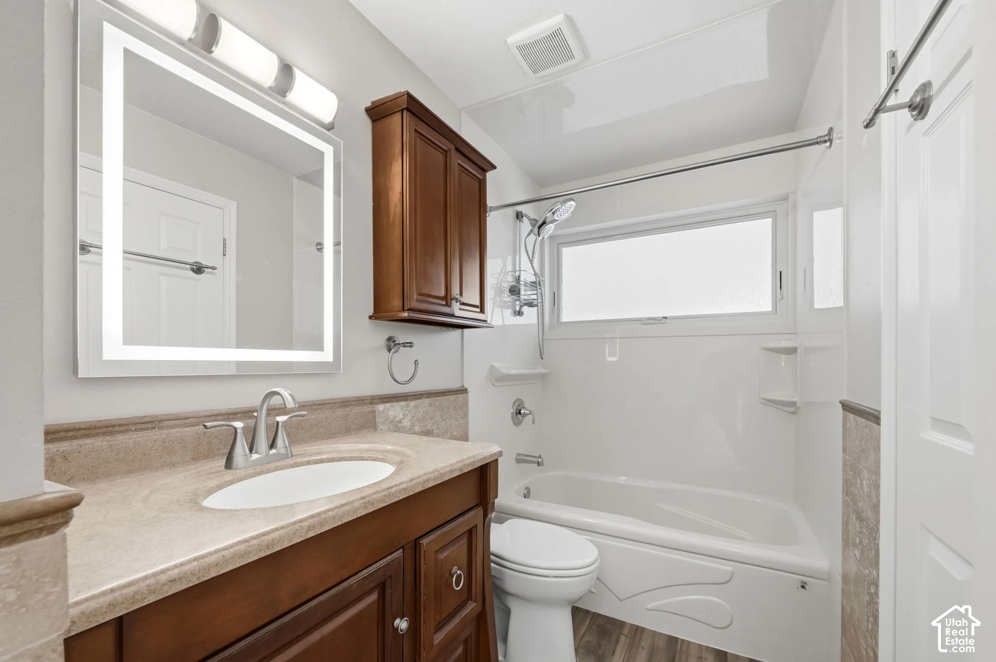 Bathroom featuring a wood-finish vanity with a stone-surface countertop, an integrated LED-backlit mirror, a wall-mounted wooden cabinet, and a shower-tub combination with a polished metal faucet