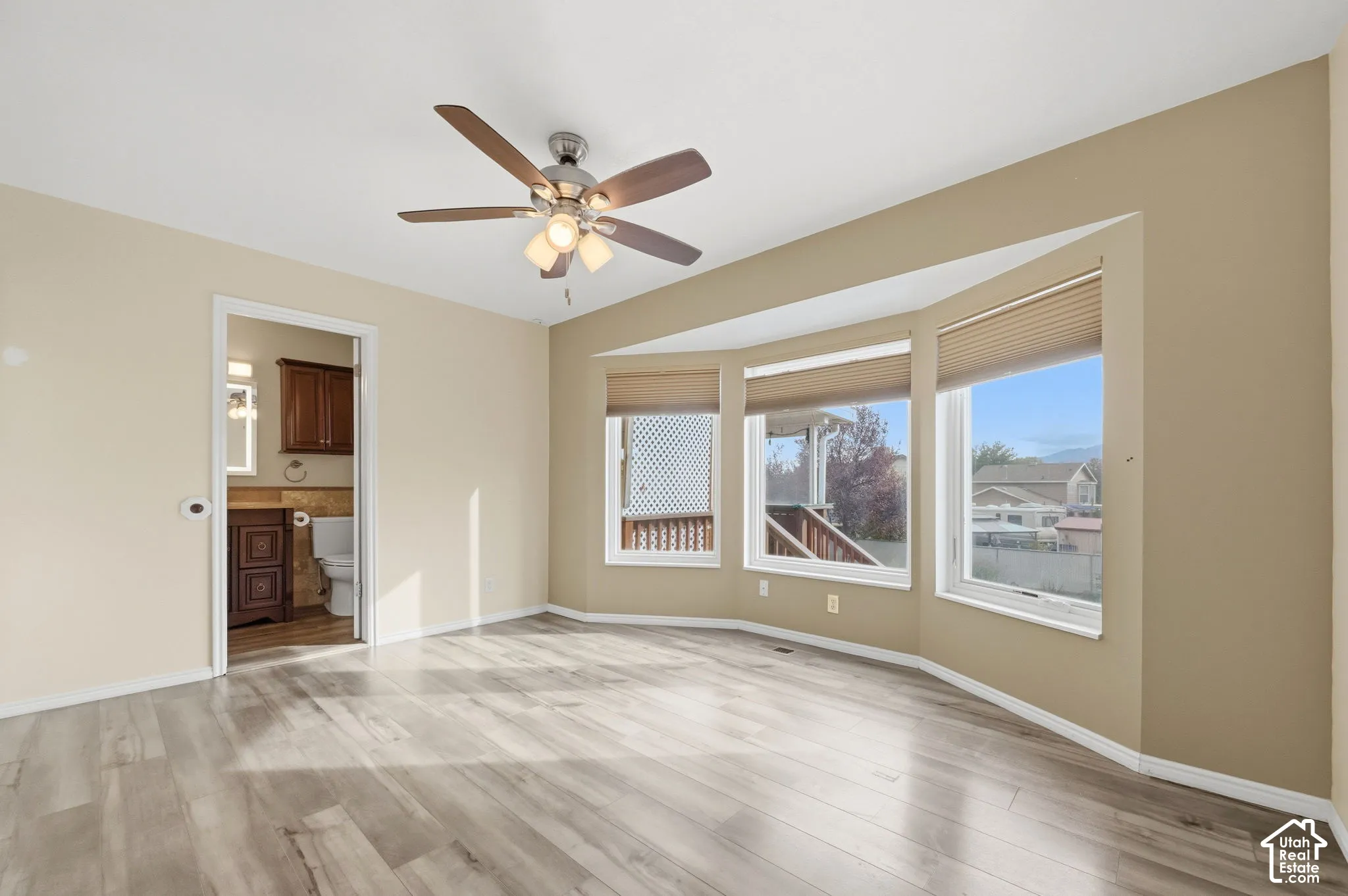 Bay window featuring pleated cellular shades, wood-finish flooring, ceiling fan with integrated light fixture, and neutral wall tones