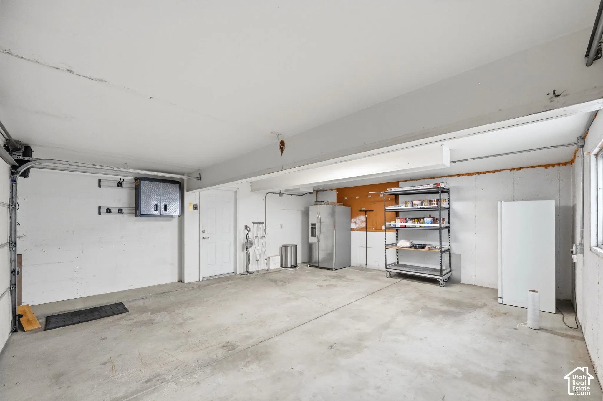 Finished garage featuring smooth concrete flooring, exposed structural beams, high-output overhead lighting, and white paneled interior access door
