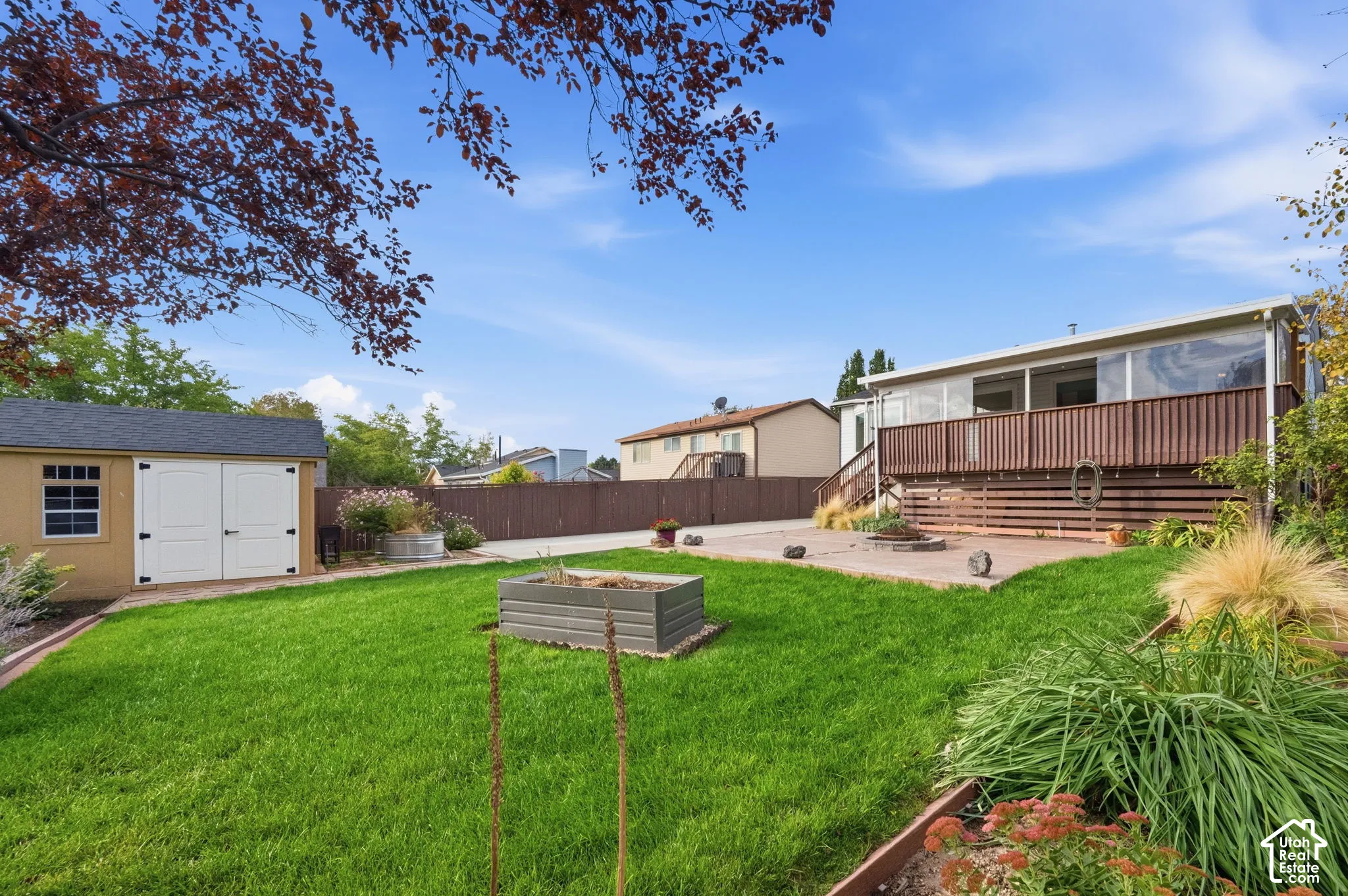 Backyard featuring a wood deck, concrete patio, detached storage shed, raised garden bed, and perimeter fencing