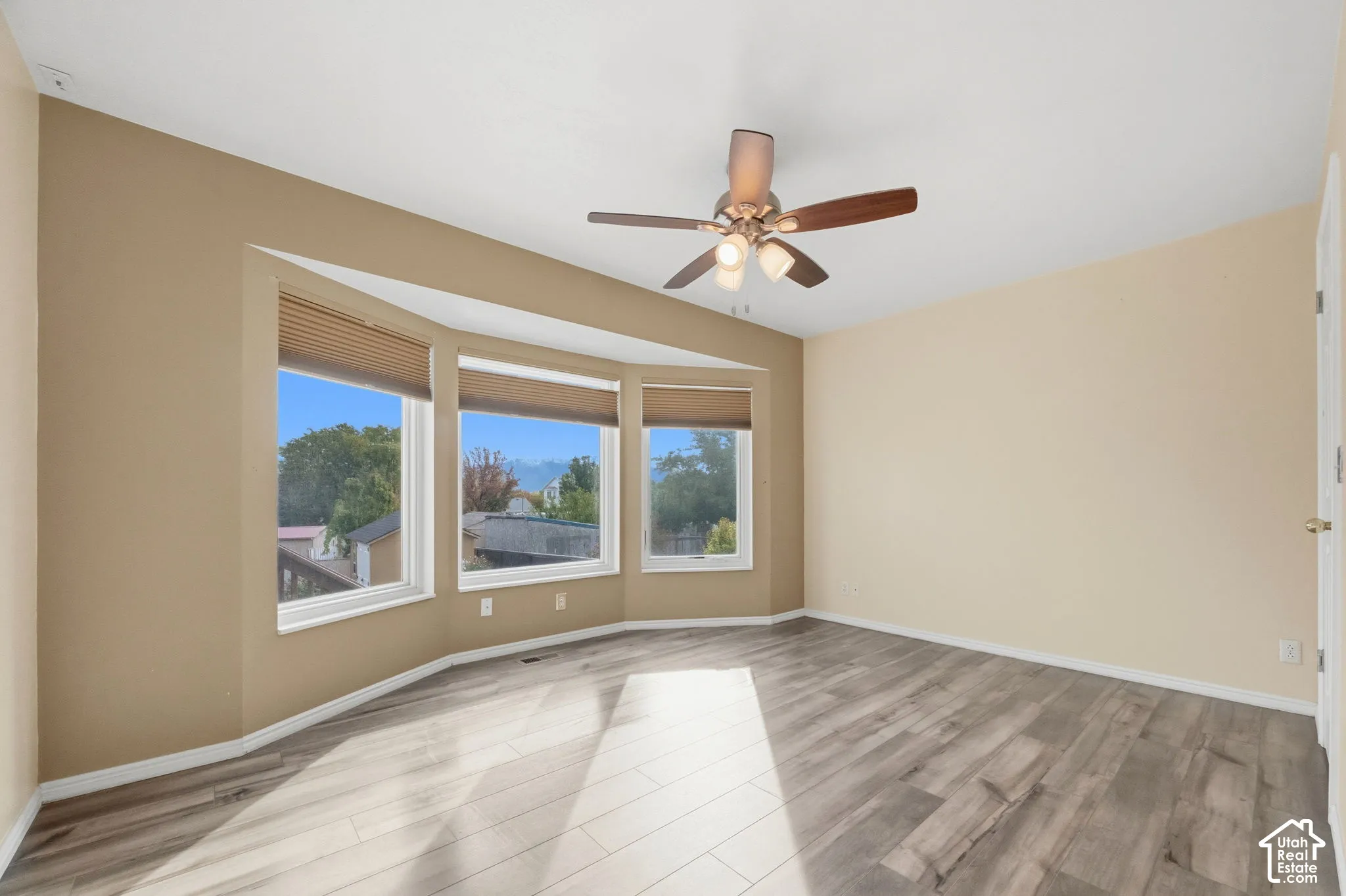 Bay window featuring three individual window panes, wood-finish flooring, and a ceiling-mounted light fixture with a fan