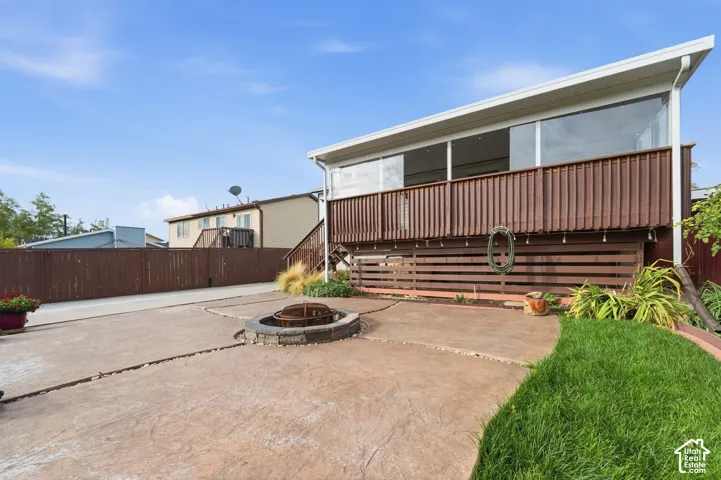 Stamped concrete patio featuring a built-in stone fire pit, wood-finish privacy fencing, and an elevated glass-enclosed deck