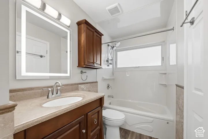 Bathroom featuring a wood-finish vanity with a stone-surface countertop, an integrated LED-backlit mirror, a wall-mounted wooden cabinet, and a shower-tub combination with a polished metal faucet
