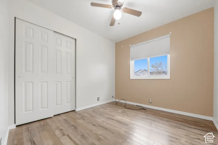 Room featuring wood-finish flooring, a sliding-door closet, neutral-toned walls, and a ceiling-mounted light fixture with a fan