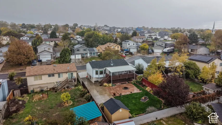 Aerial perspective of the property featuring a rear wood deck, paved patio, manicured lawn, and detached storage structure