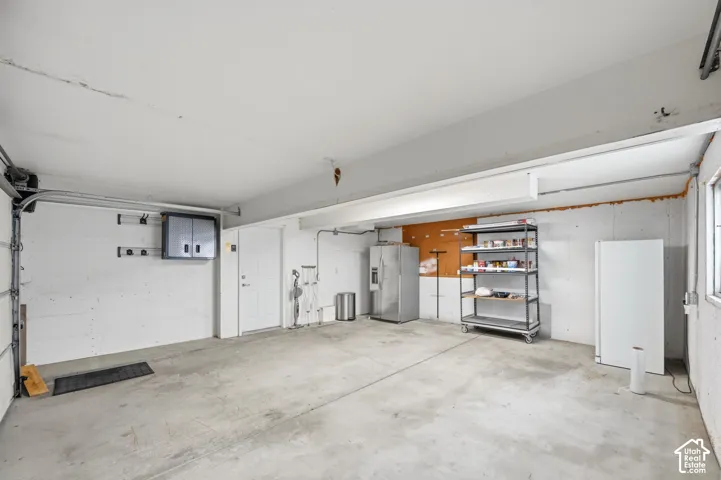 Finished garage featuring smooth concrete flooring, exposed structural beams, high-output overhead lighting, and white paneled interior access door