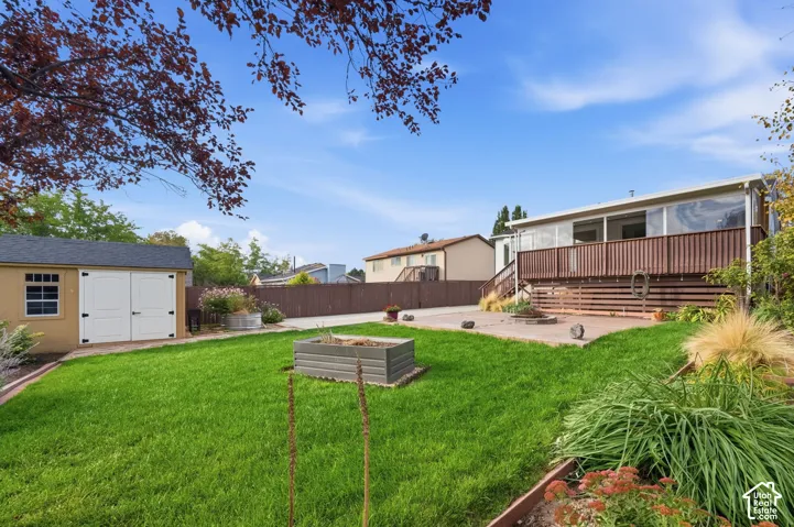 Backyard featuring a wood deck, concrete patio, detached storage shed, raised garden bed, and perimeter fencing