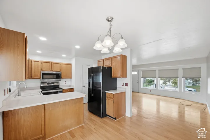 Kitchen featuring light wood-finish cabinetry, stainless steel microwave, and wood-finish flooring, complemented by a multi-light chandelier