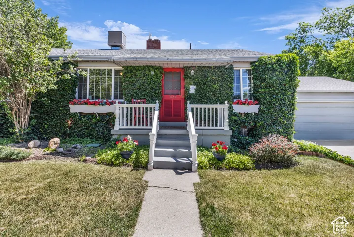 Exterior facade featuring a red front door, white balustrade entry steps, window boxes, and stone siding partially covered in climbing ivy