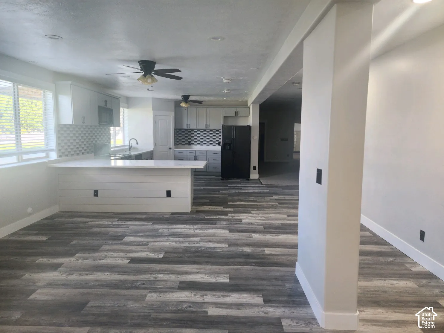 Kitchen featuring white cabinetry, quartz countertops, a shiplap-accented island, geometric tile backsplash, and wood-finish flooring