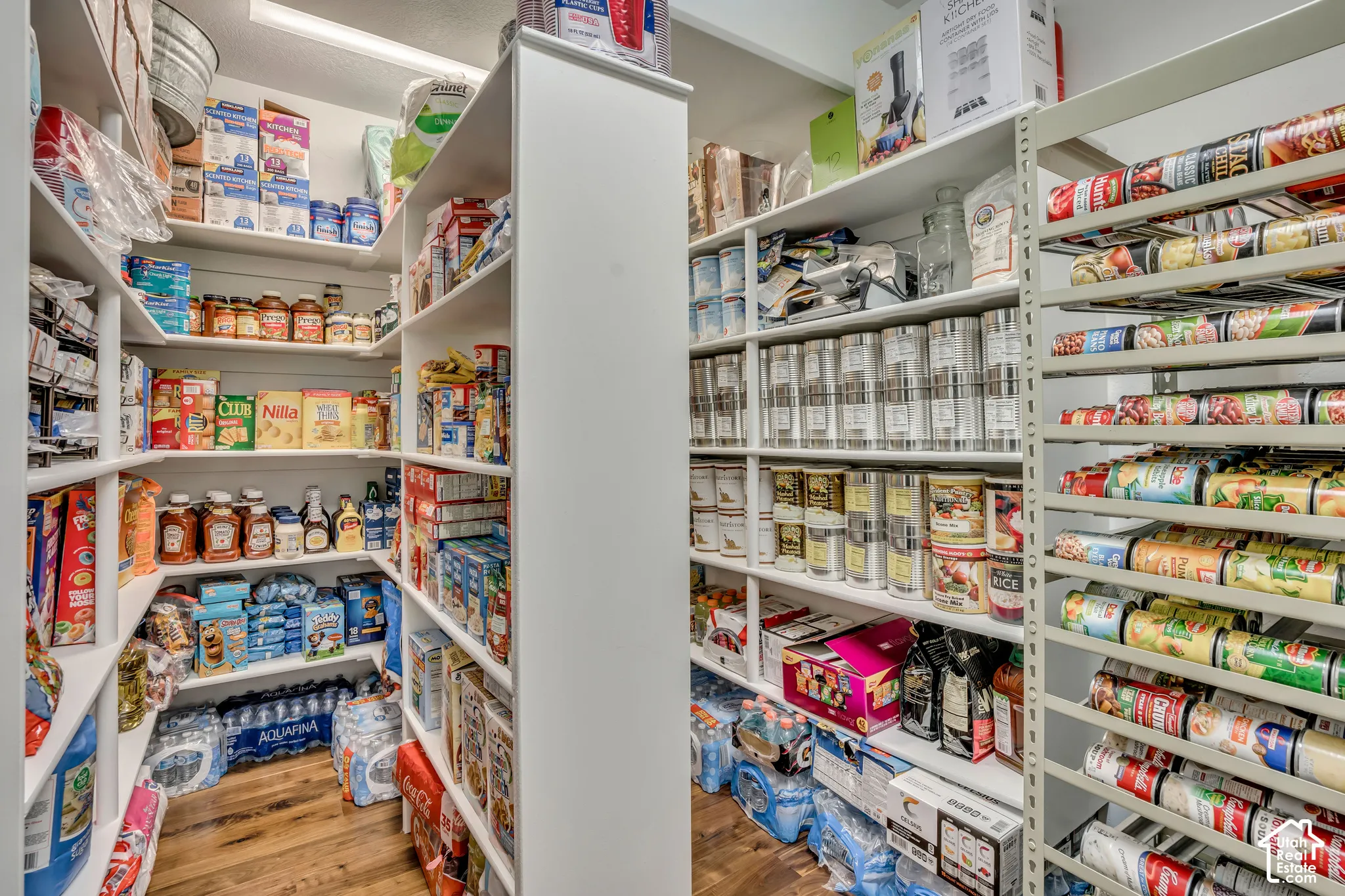 Walk-in pantry featuring custom white floor-to-ceiling shelving, adjustable storage racks, and wood-finish flooring
