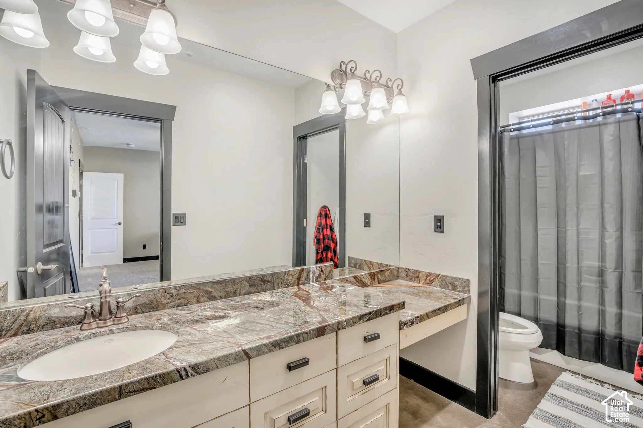 Vanity featuring a stone countertop, oval undermount sink, cream-colored cabinetry with dark hardware, and dual wall-mounted light fixtures