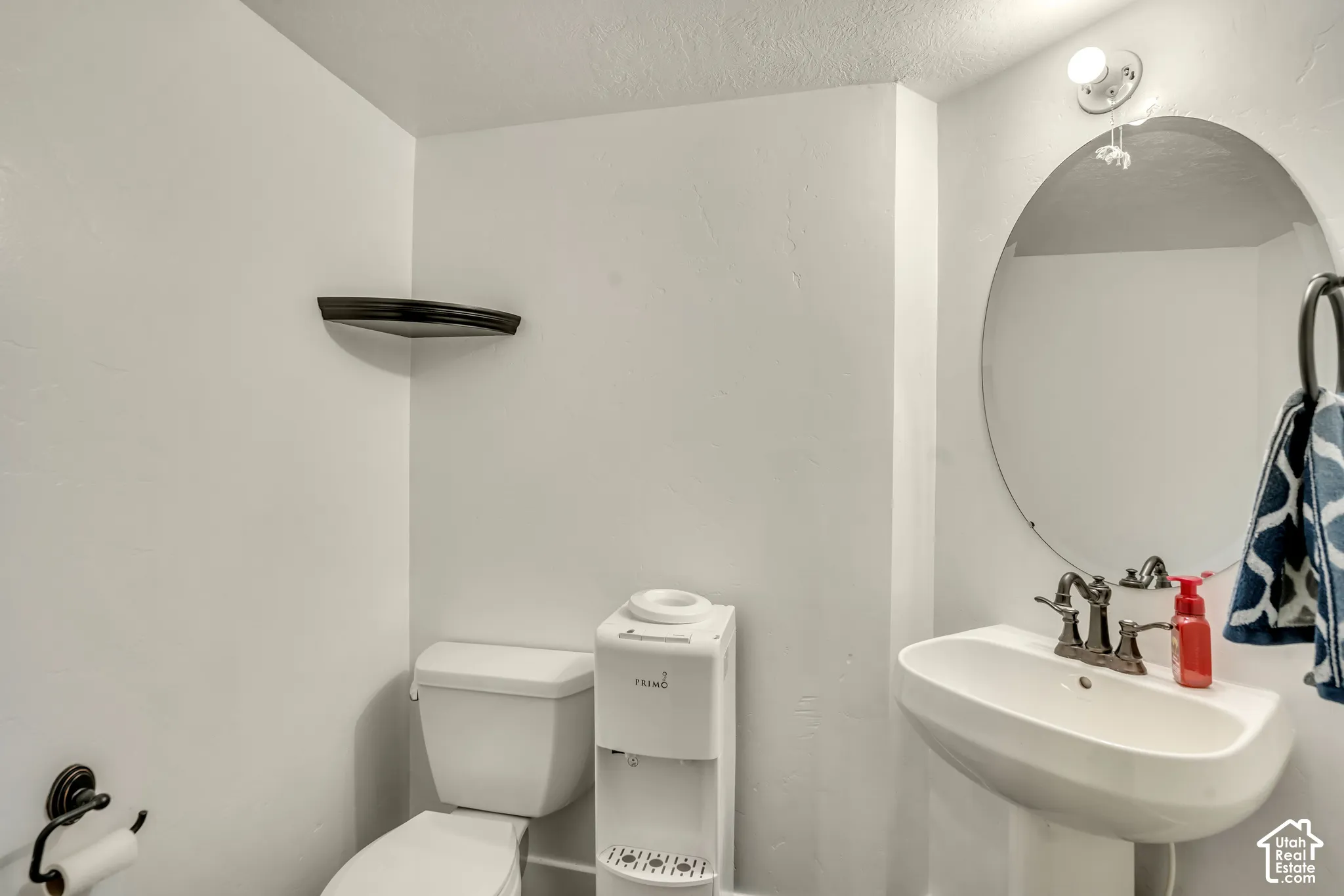 Wall-mounted oval mirror, pedestal sink with multi-handle faucet, built-in corner shelving, and oil-rubbed bronze hardware